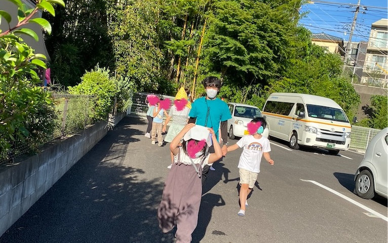 畑からの帰り道を歩く子どもたちと、奥に停めた白いワゴン車